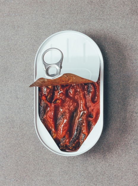 Open canned sprats in tomato sauce on a gray background close-up view from above. tinted photo