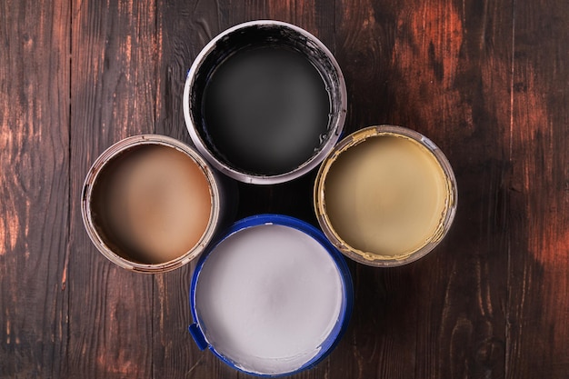 Open cans with whiteblackbrown and yellow paint on wooden background top view