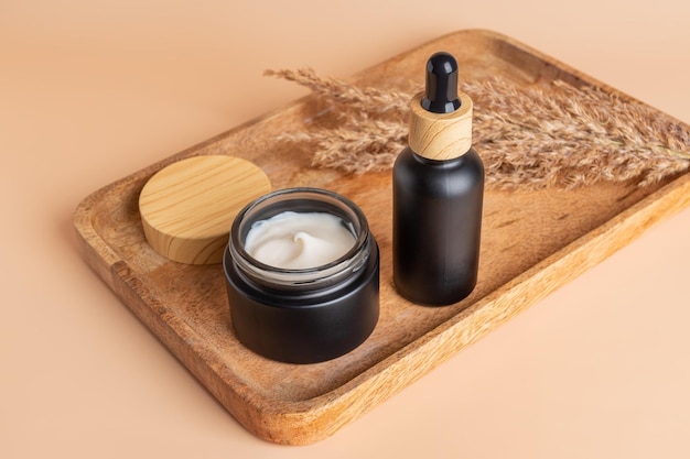 Open cream jar and dropper bottle with face oil on a wooden tray Cosmetic container mockups Background for branding and packaging presentation Natural skincare beauty product concept