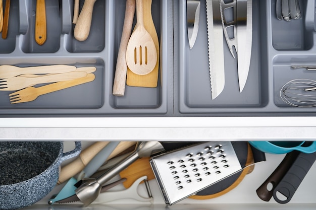 Open drawer with different utensils and cutlery in kitchen, flat lay.