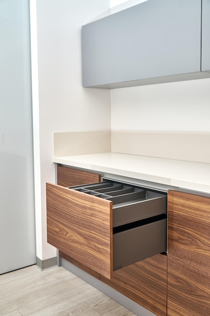 Open drawers with cutlery tray in kitchen of walnut wood with acrylic solid surface countertop