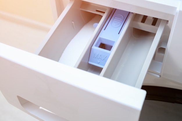 Open empty detergent drawer of modern washing machine standing on wooden floor at home close view