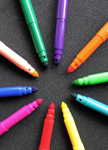 Open felttip pens of different colors in the shape of a star lie on a black background vertical pho