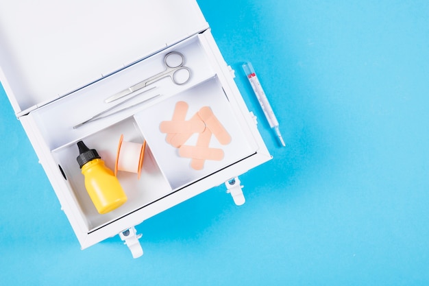 An open first aid kit with syringe on blue background