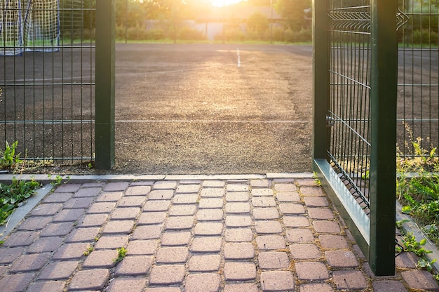 Open gates on a sports ground fenced with a welded mesh fence outdoors in the evening at sunset