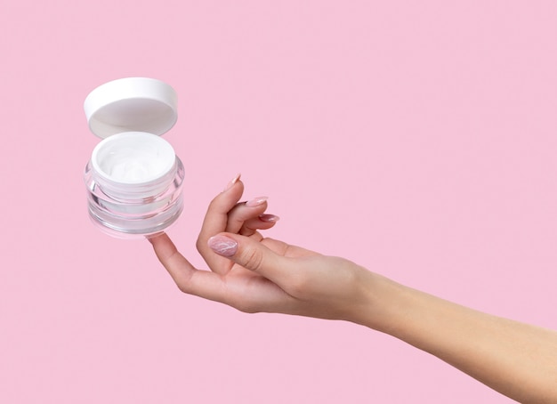 Open jar with cosmetic cream with woman hand.