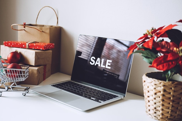 Open laptop computer with word sale on display screen poinsettias christmas flower and gift boxes on