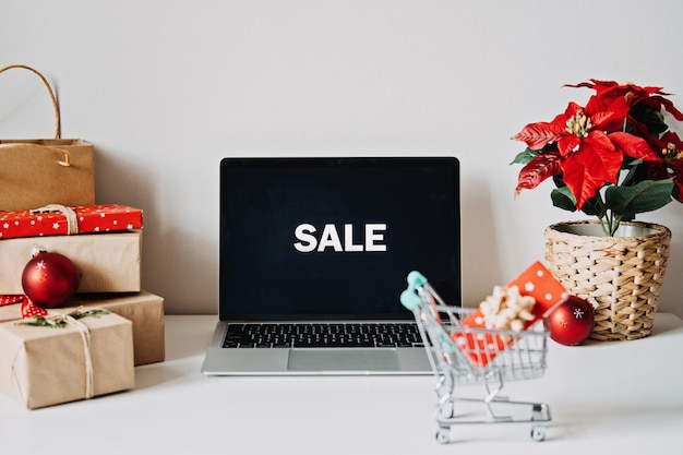 Open laptop computer with word sale on display screen poinsettias christmas flower and gift boxes on