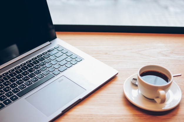 Open laptop and a Cup of coffee on the table in the cafe, freelance concept