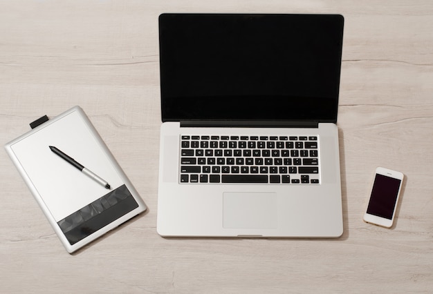 Open the laptop, graphics tablet and smart phone on a light table, top view