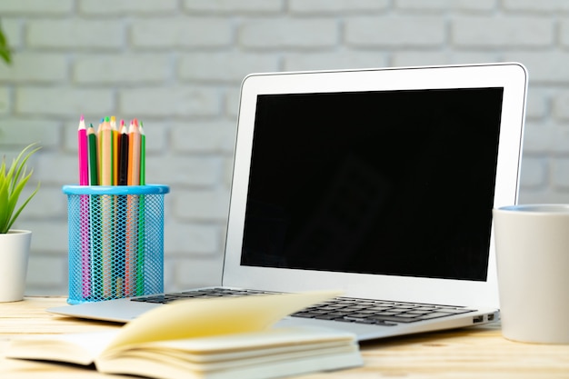 Open laptop with notepad and heap of pencils on wooden desk