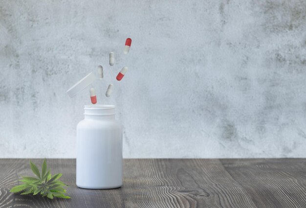 Open medicine bottle with pills in the air and cannabis plant