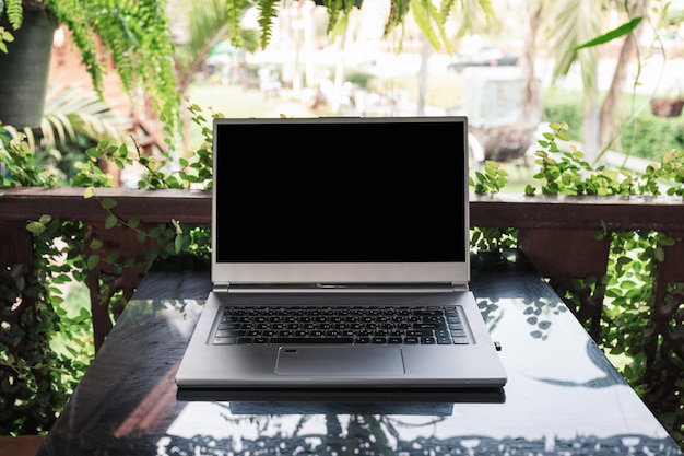 Open modern gray laptop on glass table in spring garden on sunny