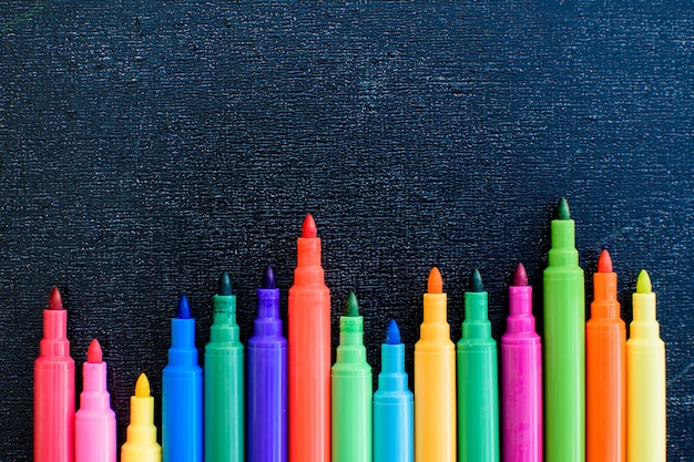 Open multicolored markers closeup on black board background Place for text