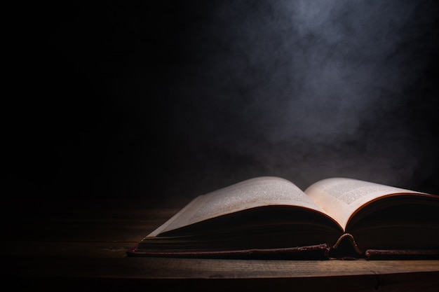 Open a mysterious old book on wooden table, smoke float up from book