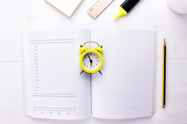 An open notebook with an alarm clock and office supplies