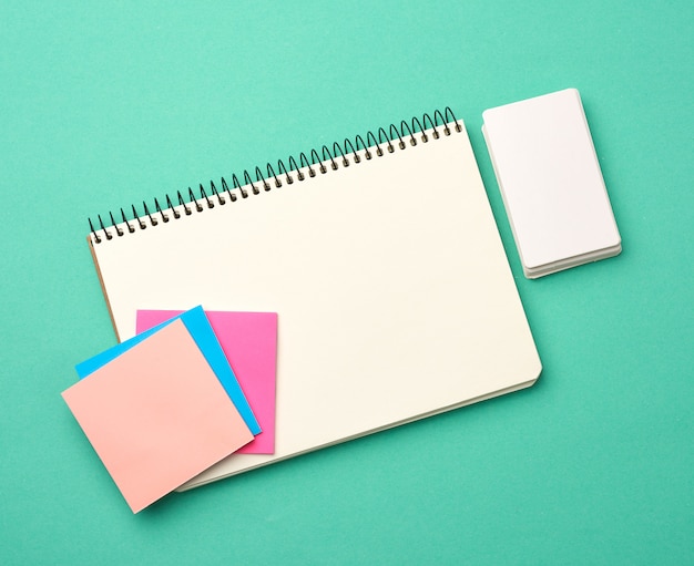 Open notebook with blank white sheets, color stickers and rectangular business cards on a green background