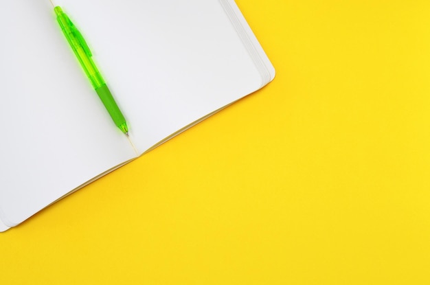 open notebook with blank white sheets and a pen on a yellow background