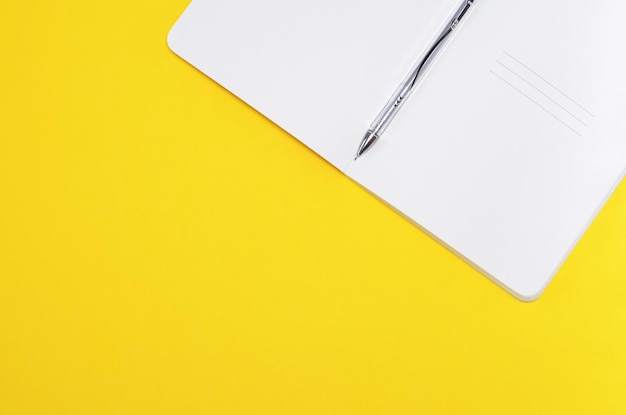 Open notebook with a pen on a yellow background copy space