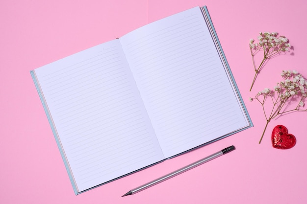 Open notebook wooden pencil on pink background top view