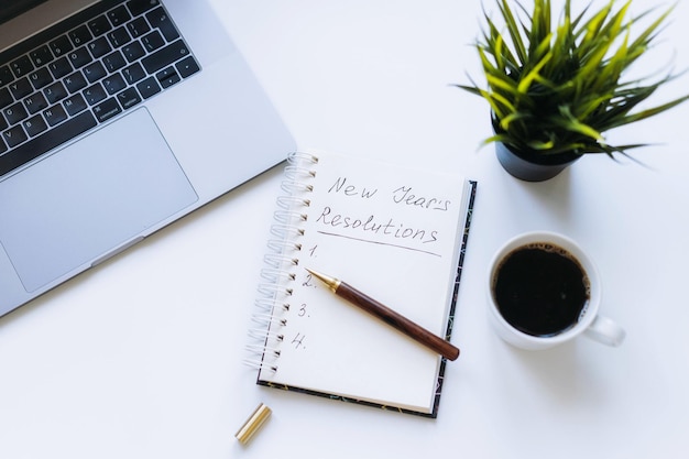 Open notepad with new year resolutions and empty list Flower laptop and coffee cup on background