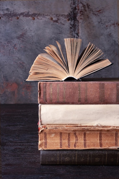 An open novel lies on a stack of old books on a brown background