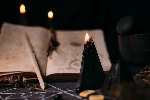 Open old book with magic spells, runes, black candles on witch table. Occult, esoteric, divination and wicca concept. Halloween scene