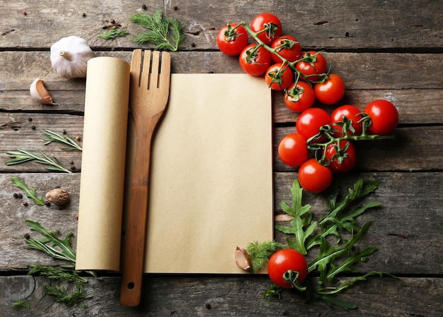 Open recipe book with fresh herbs tomatoes and spices on wooden background