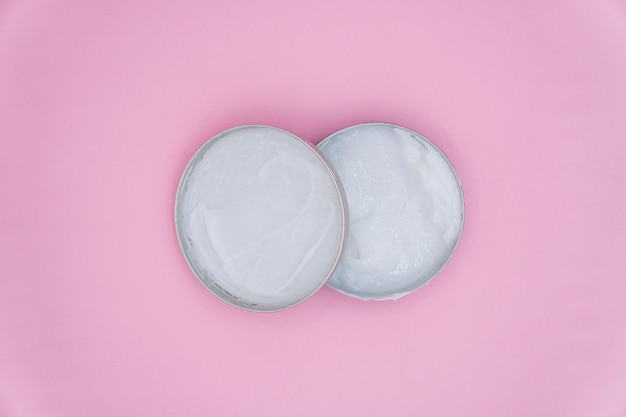 Open round jar of white cream. Cosmetic product for skin care. Top view on a pink background.