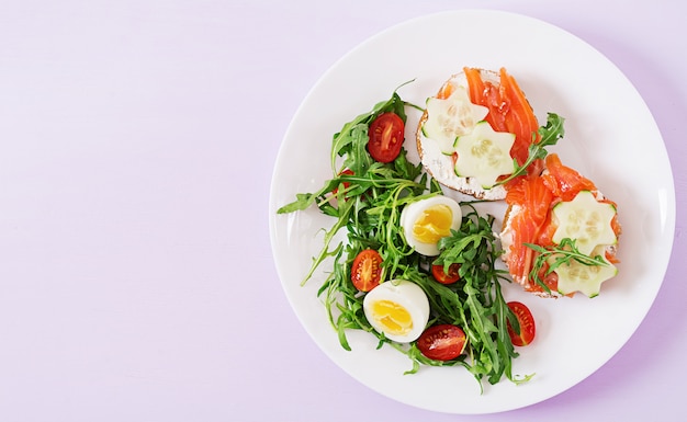  Open sandwiches with salmon, cream cheese and rye bread in a white plate and salad 