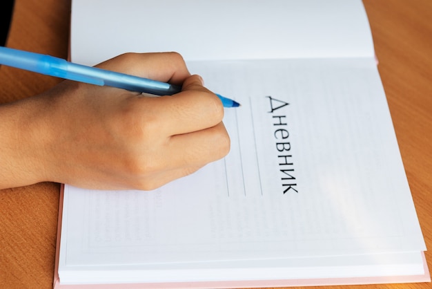 An open school diary and a child's hand with a writing pen