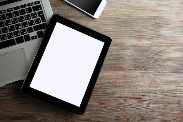 An open silver laptop mobile phone and modern tablet on the wooden background