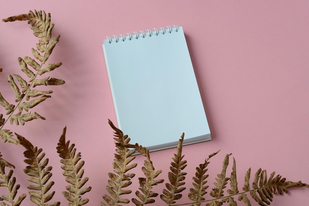 Open spiral notepad and dry tropical fern leafs on a soft pink background Flat lay with copy space