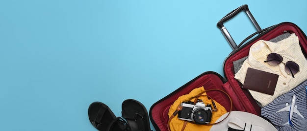 Open suitcase with camera sunglasses passport and clothes on blue background Preparing for the summer vacations