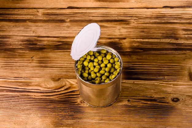 Open tin can with green pea on wooden table