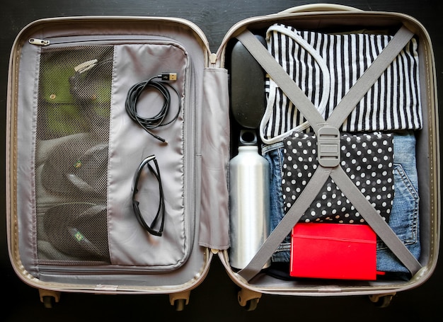 Open travel suitcase full of clothes isolated on black background