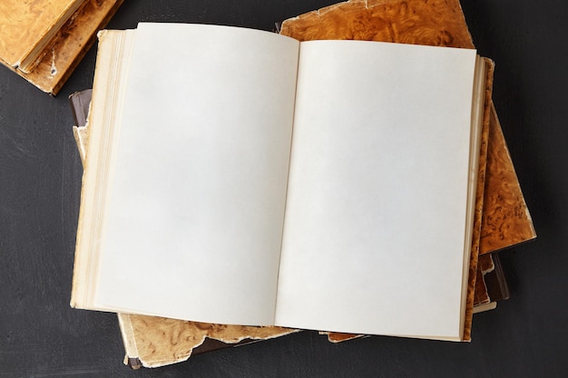 Open vintage book or notebook in a dust jacket on a stack of old shabby books on a dark concrete table