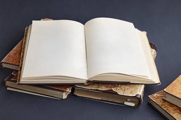 Open vintage book or notebook in a dust jacket on a stack of old shabby books on a dark concrete table