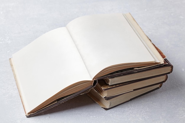 Open vintage book with blank pages lies on a stack of old shabby books in a dust jacket on a gray concrete table Book Day Copy space mockup