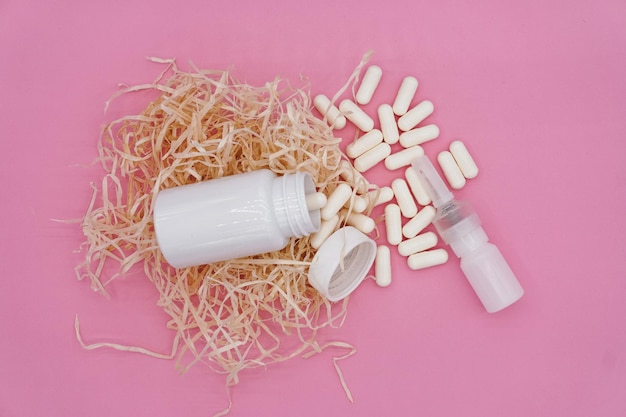 An open white plastic bottle lies on decorative hay, white capsules spilled out of the bottle