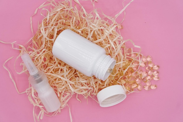 An open white plastic bottle lies on decorative hay, yellow capsules spilled out of the bottle