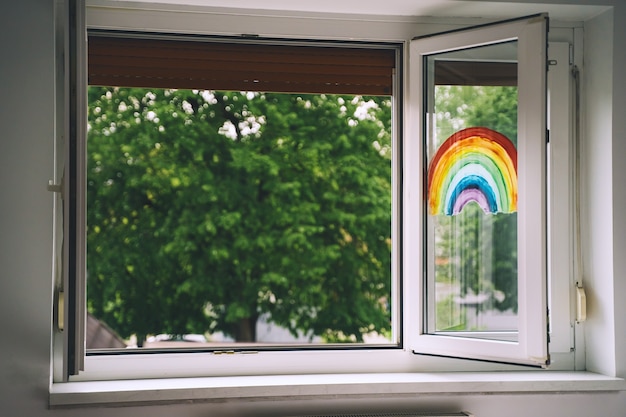 Open window in room with green trees on background Painting rainbow on window