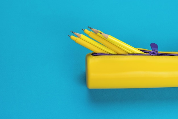 An open yellow pencil case with pens and pencils on a blue background The minimum concept of storing school supplies Flat lay