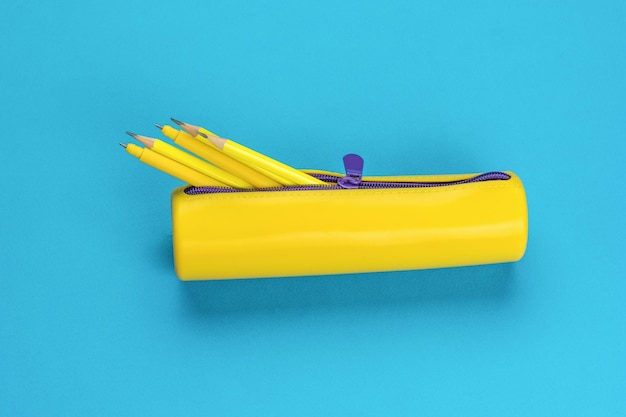 An open yellow pencil case with protruding pencils on a blue background The minimum concept of storing school supplies Flat lay