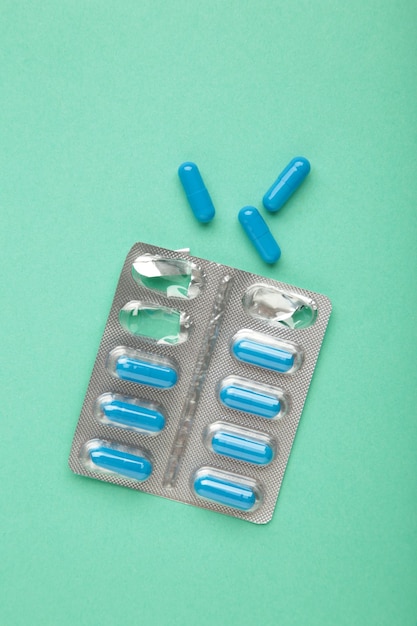 Opened blister pack with blue pills on a mint background Concept of treatment of chronic diseases Vertical photo