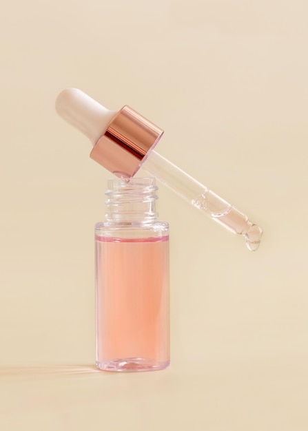 Opened Bottle with falling serum drop on light beige close up Skincare beauty product