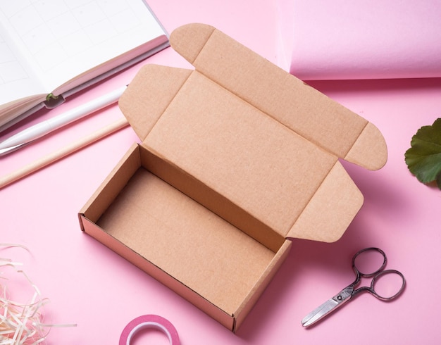 Opened cardboard carton box on pink background decorated with red flowers