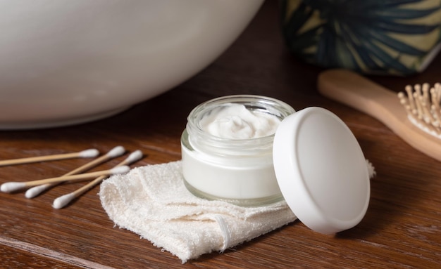 Opened cosmetic cream jar on folded towel near basin on wooden counterto in bath lid mockup