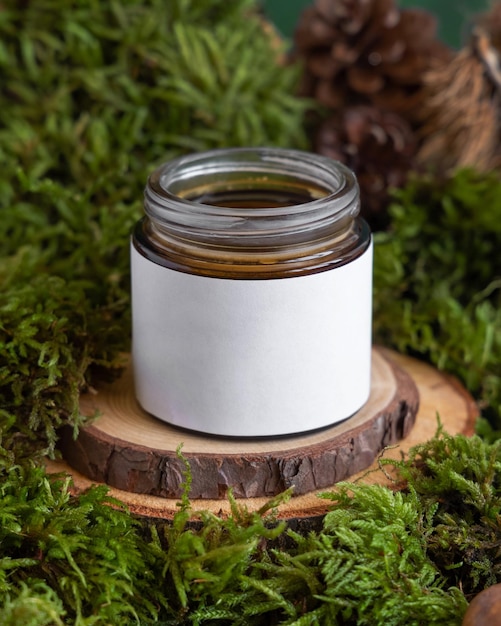 Opened cream glass jar with blank label on wooden piece between green moss closeup mockup