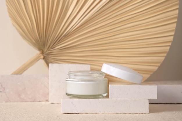 Opened cream jar on travertine stone against dry beige palm leaf close up cosmetic mockup